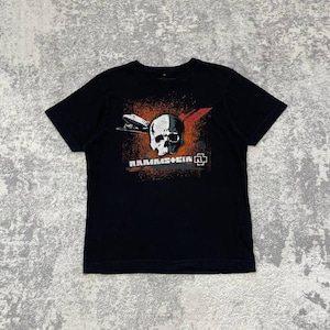 May include: Black t-shirt featuring a graphic design with a skull, a zeppelin, and the band name "Rammstein". The design incorporates red, orange, and white elements. The shirt is a classic crew neck style.