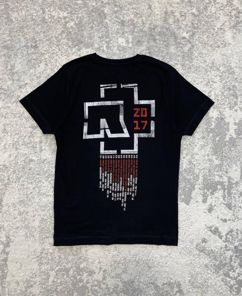 K&ouml;nnte beinhalten: Ein schwarzes Kurzarm-T-Shirt mit einer gro&szlig;en wei&szlig;en und roten Grafik auf der R&uuml;ckseite. Das Design enth&auml;lt ein stilisiertes Logo, den Text 20 17 und eine Liste von Tourdaten und Orten, die in wei&szlig;er und roter Schrift unter der Grafik stehen.