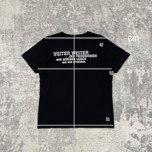 May include: Black t-shirt with white text that reads "WEITER WEITER INS VERDERBEN WIR M&Uuml;SSEN LEBEN BIS WIR STERBEN." The shirt measures 64 cm across the chest, 52 cm in length, 51 cm at the bottom, and 42 cm from the collar to the shoulder. The shirt is displayed on a gray surface.