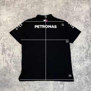 May include: Black polo shirt with the word "PETRONAS" in white across the back. The shirt has short sleeves and a collar. Measurements are shown in centimeters: 79 cm across the shoulders, 51 cm from shoulder to sleeve, 63 cm from shoulder to hem, and 64 cm across the bottom.