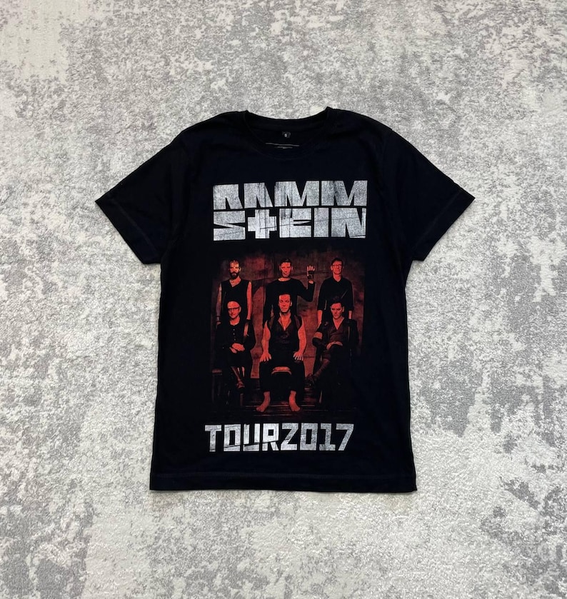 K&ouml;nnte beinhalten: Ein schwarzes Kurzarm-T-Shirt mit dem Bandnamen RAMMSTEIN in einer abgenutzten silbernen Schriftart oben. Unter dem Text befindet sich ein dunkles, stimmungsvolles Foto der sechs Bandmitglieder. Die Worte TOUR 2017 sind unten in Silber gedruckt.