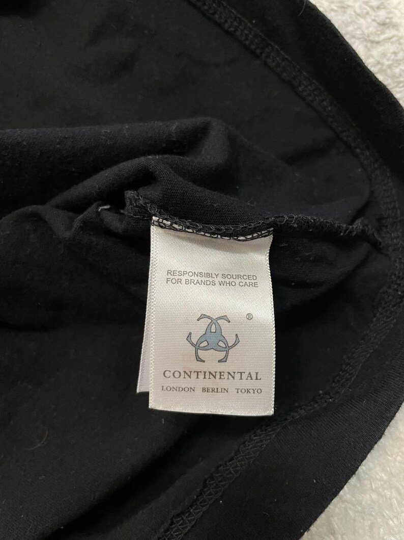 K&ouml;nnte beinhalten: Ein schwarzes Kleidungsst&uuml;ck mit einem wei&szlig;en, rechteckigen Etikett am Halsausschnitt. Das Etikett zeigt den Text RESPONSIBLY SOURCED FOR BRANDS WHO CARE, ein kreisf&ouml;rmiges Logo und den Markennamen CONTINENTAL mit LONDON BERLIN TOKYO darunter.