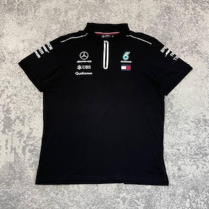 May include: Black polo shirt with a white zipper and collar trim. Features logos for AMG, UBS, Qualcomm, and Petronas. Short sleeves with sponsor logos. A sporty, casual top.