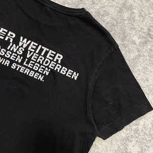 May include: Black t-shirt with white text. The text reads "ER WEITER INS VERDERBEN MUSSEN LEBEN WIR STERBEN." The shirt has a crew neck and short sleeves. The fabric appears to be cotton or a cotton blend.