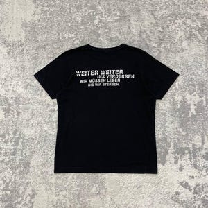 May include: Black t-shirt with white text on the back. The text reads "WEITER WEITER INS VERDERBEN WIR M&Uuml;SSEN LEBEN BIS WIR STERBEN."