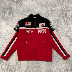 May include: Red, black, and white Ferrari racing jacket with a stand-up collar. The jacket features the Ferrari logo, sponsor patches, and the word "Ferrari" in large white letters across the chest. The sleeves have white stripes.
