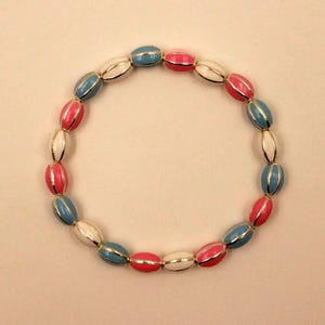Puede incluir: Un brazalete colorido con cuentas ovaladas en colores alternos blanco, rosa y azul. Las cuentas están acentuadas con metal dorado y ensartadas para formar una forma circular. Un accesorio elegante.