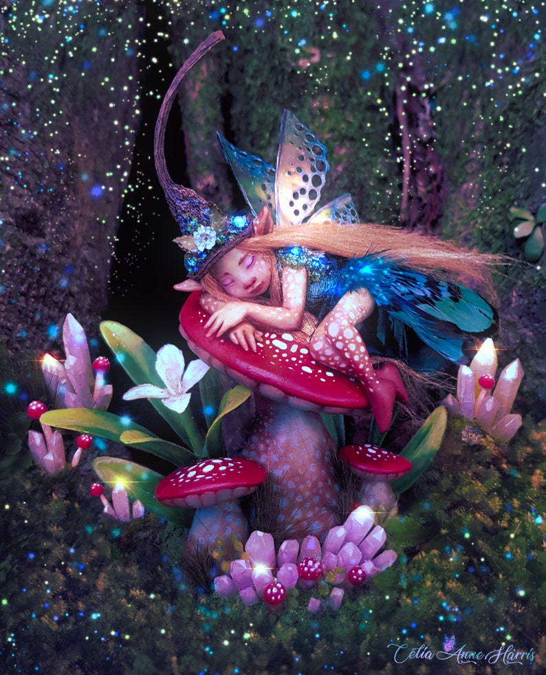 May include: A figurine of a sleeping fairy with long blonde hair, wearing a tall pointed hat and blue wings, resting on a large red mushroom with white spots. The scene includes clusters of light pink crystals and a white flower.