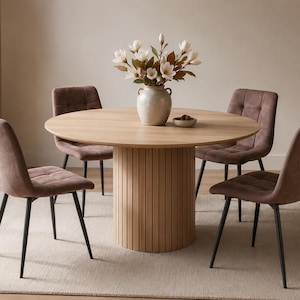 May include: A light oak dining table with a circular top and a fluted base, accompanied by four upholstered chairs. The chairs and table are set on a neutral rug. A vase of flowers is on the table.