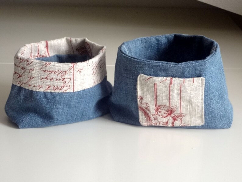 Peut inclure: Deux paniers de rangement en tissu bleu avec une doublure en tissu blanc. Un panier a un patch en tissu blanc avec un motif d'ange rouge. L'autre panier a une doublure en tissu blanc avec une &eacute;criture rouge.