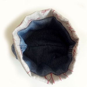 Peut inclure: Une petite pochette ronde doubl&eacute;e de denim avec un ext&eacute;rieur en tissu blanc. Le tissu a un motif d'&eacute;criture rouge.