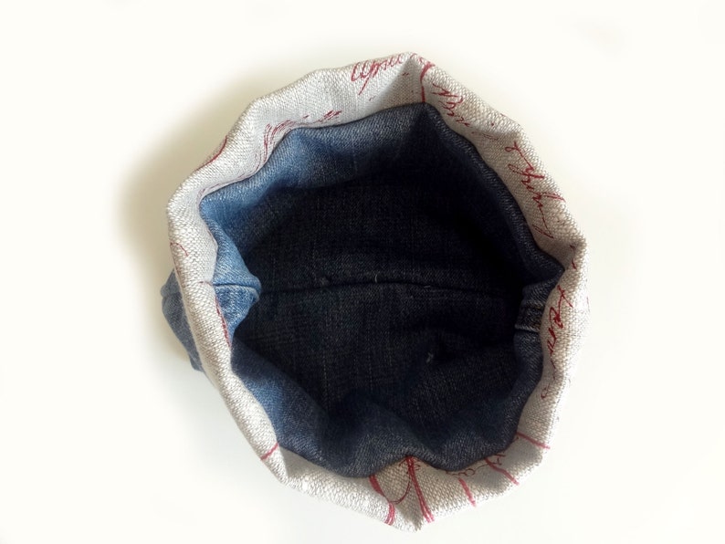 Peut inclure: Une petite pochette ronde doubl&eacute;e de denim avec un ext&eacute;rieur en tissu blanc. Le tissu a un motif d'&eacute;criture rouge.