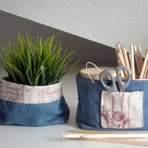 Peut inclure: Deux paniers de rangement en tissu denim avec une doublure en tissu blanc. Un panier contient une plante verte en pot et l'autre contient des crayons et une paire de ciseaux.