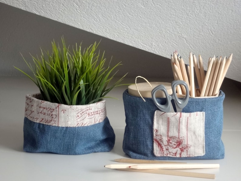 Peut inclure: Deux paniers de rangement en tissu denim avec une doublure en tissu blanc. Un panier contient une plante verte en pot et l'autre contient des crayons et une paire de ciseaux.