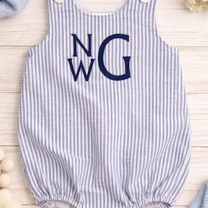 Puede incluir: Romper de bebé a rayas azules y blancas con las iniciales "NWG" bordadas. El romper sin mangas tiene botones en los hombros y corchetes en la parte inferior. La tela tiene una textura de seersucker.