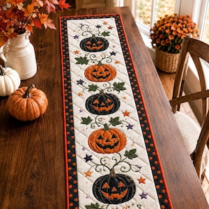 May include: A rectangular quilted table runner featuring a cream-colored center panel with an alternating pattern of black and orange jack-o'-lanterns, green leaves, and small colorful stars, bordered by a black fabric with orange polka dots.