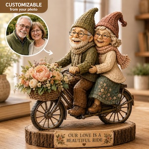 May include: A figurine of an elderly couple riding a bicycle, featuring a basket of flowers, set on a wooden base with the text 'OUR LOVE IS A BEAUTIFUL RIDE'. An inset shows a customizable photo of a couple, with the text 'CUSTOMIZABLE from your photo'.