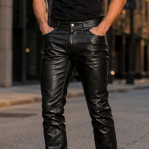 Op de afbeelding: Een zwart T-shirt met korte mouwen en ronde hals gecombineerd met een zwarte leren broek met knoop- en ritssluiting, gedragen met zwarte leren laarzen en een donker getinte zonnebril voor een monochrome outfit met een gladde afwerking.