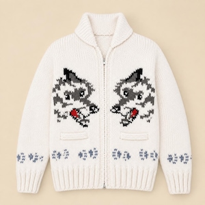 May include: A cream-colored knit zip-up cardigan featuring a shawl collar and two front pockets. The garment displays two symmetrical wolf head designs in gray, black, and red, with small gray paw print patterns along the hem and sleeves.