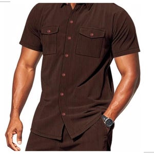 May include: Brown short-sleeved shirt with two chest pockets and matching pants. The shirt has a button-down front and a classic collar. The fabric has a vertical ribbed texture. The outfit is a solid brown color.