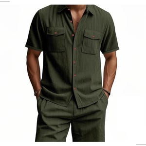 May include: Olive green short-sleeved shirt and matching pants set. The shirt has two chest pockets and red buttons. The fabric has a vertical striped texture. The outfit is a casual, coordinated ensemble.