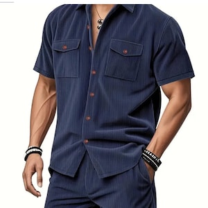 May include: Navy blue short-sleeve shirt and matching pants. The shirt has two chest pockets and brown buttons. The fabric has a vertical ribbed texture. The outfit is a coordinated set.