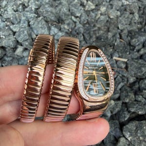Puede incluir: Un reloj Bvlgari Serpenti de oro rosa con una caja en forma de cabeza de serpiente y un bisel engastado con diamantes. El reloj cuenta con una pulsera flexible tipo tubogas de varias vueltas y una esfera oscura con patrón guilloché.