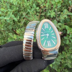 Puede incluir: Un reloj Bvlgari Serpenti con esfera verde en forma de lágrima, índices plateados, números romanos en las doce y las seis, y un bisel de oro rosa con diamantes. El brazalete flexible presenta eslabones alternos de oro rosa y acero inoxidable.