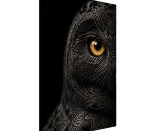 May include: A vertical canvas print featuring a close-up, high-contrast portrait of an owl. The owl has dark, textured, charcoal-colored feathers and a single, piercing, bright amber-yellow eye set against a deep black background.