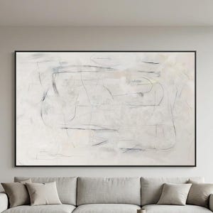 Puede incluir: Gran pintura abstracta enmarcada en negro. La obra presenta una paleta de colores neutros con tonos suaves de blanco, beige y gris. Delicadas líneas y formas negras crean la composición. El cuadro cuelga sobre un sofá gris claro.