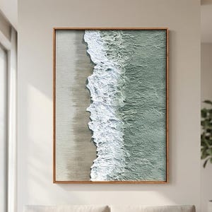 Puede incluir: Una obra de arte enmarcada que representa una escena costera. La imagen muestra una sección de playa con olas rompiendo en la orilla. La obra de arte está enmarcada en un marco de madera y cuelga sobre un sofá beige en una sala de estar moderna.