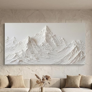 Pode incluir: Uma grande obra de arte texturizada de uma cordilheira branca está pendurada acima de um sofá bege. A obra de arte apresenta um relevo detalhado de picos e vales. A sala inclui uma mesa de centro, almofadas e um tapete, criando um espaço de convivência moderno em tons neutros.