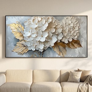 Könnte beinhalten: Gerahmtes Wandkunstwerk mit weißen Hortensienblüten und goldfarbenen Blättern. Das Kunstwerk hat eine strukturierte, dreidimensionale Optik und ist vor einem hellgrauen Hintergrund platziert. Der Rahmen ist schwarz.