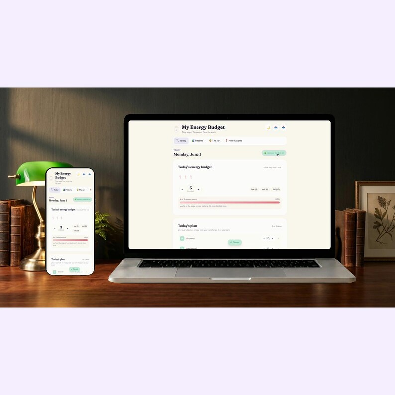 A laptop and phone displaying the My Energy Budget app, resting on a calm wooden desk next to a small plant.