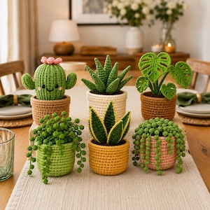May include: A collection of six crocheted potted plants arranged on a table. The set includes a smiling cactus with pink flowers, a spiky succulent, a monstera, a snake plant, and two hanging string of pearls plants in various colored pots.