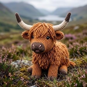 May include: A crocheted Highland cow figurine with brown and tan yarn. The cow has long, shaggy fur, large horns, and is sitting in a field of purple flowers and green grass. The background features a lake and mountains.