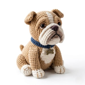 May include: A crocheted bulldog dog in shades of tan, cream, and brown, with a blue collar and a bone-shaped tag. The handmade stuffed animal is sitting, with detailed features and a friendly expression.