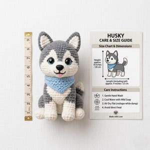 Pode incluir: C&atilde;o husky de croch&ecirc; com detalhes cinza, branco e azul. O brinquedo de pel&uacute;cia tem olhos azuis e uma bandana azul. A altura &eacute; de aproximadamente 20 cm e o comprimento de aproximadamente 23 cm. Um guia de cuidados est&aacute; inclu&iacute;do.