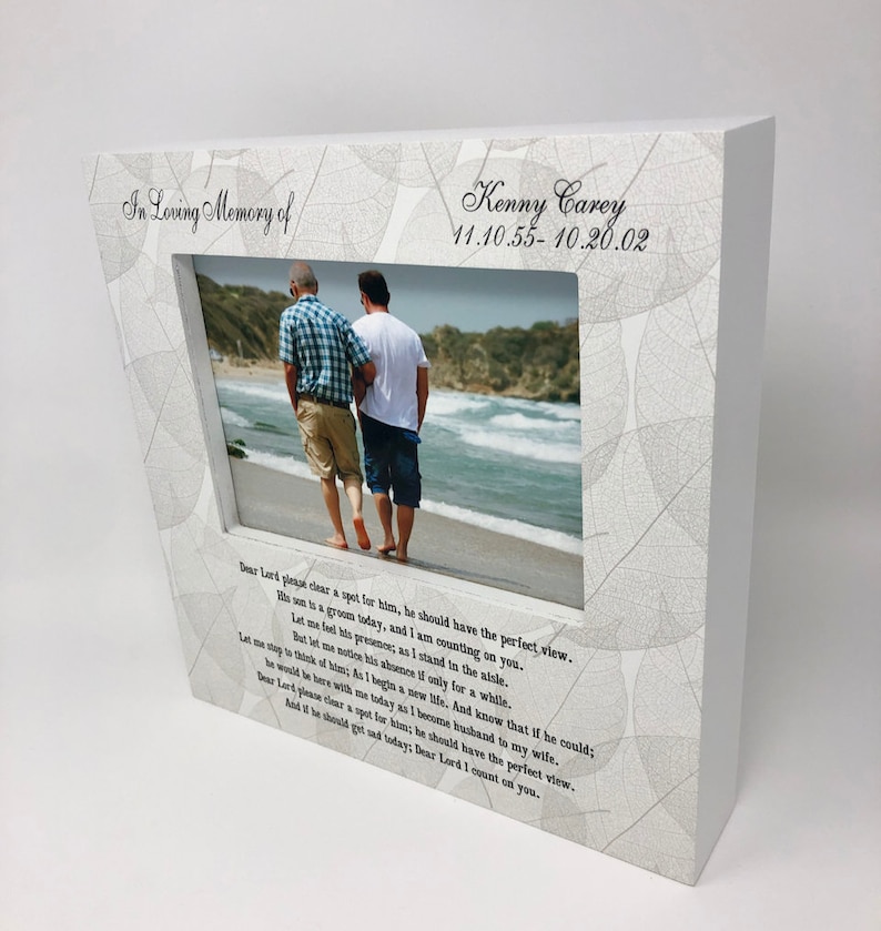 May include: White wooden picture frame with a white and gray leaf pattern. The frame has a photo of two people walking on a beach. The text "In Loving Memory of Kenny Carey 11.10.55-10.20.02" is printed on the frame. The text "Dear Lord please clear a spot for him, he should have the perfect view. His son is a groom today, and I am counting on you. But let me feel his presence; as I stand in the aisle. Let me not think of him; As I begin a new life. And know that if he could; he would be here with me today as I become husband to my wife. Dear Lord please clear a spot for him; he should have the perfect view. And if he should get sad today, Dear Lord I count on you." is printed below the photo.