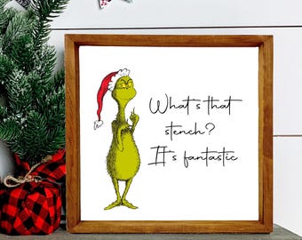 May include: A framed print featuring the Grinch wearing a Santa hat. The text reads "What's that stench? It's fantastic."