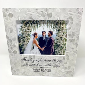 May include: A white picture frame with a floral design and a wedding photo inside. The text "Thank you for being the one who united us on this day." is printed below the photo. The names "Andrew & Kristina" and the date "October 30th, 2022" are printed below the text.