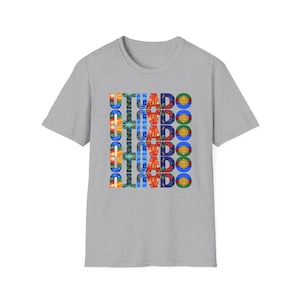 May include: A heather gray t-shirt with the word "UTUADO" vertically repeated six times in a colorful design. The design incorporates floral and circular elements in various colors.