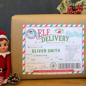 May include: A brown paper package featuring a rectangular sticker labeled ELF DELIVERY FROM THE NORTH POLE. The sticker includes a North Pole surveillance stamp, a barcode, and delivery details for Oliver Smith. A small elf doll sits beside the package.