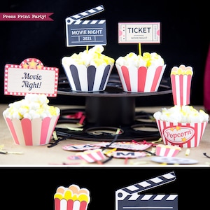 Peut inclure: Décorations de cupcakes pour une soirée cinéma avec des caissettes à cupcakes à rayures rouges et blanches. Les décorations représentent un seau de pop-corn, un billet de cinéma et une claquette avec le texte "Soirée cinéma 2021".
