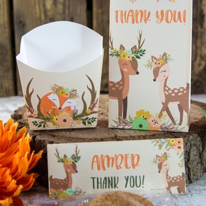 May include: A set of party favor boxes with a woodland theme. The boxes feature a fox and deer with floral crowns. The boxes are decorated with a brown, orange, and green color scheme. The boxes are labeled with the text "Thank You!" and "Amber Thank You!"
