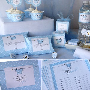 K&ouml;nnte beinhalten: Blaue und wei&szlig;e Babyparty-Dekorationen mit einem W&auml;scheleine-Thema. Die Dekorationen beinhalten Cupcakes, Geschenkboxen, eine Wasserflasche und eine Spielkarte. Der Text auf den Dekorationen lautet "Debby's Baby Shower".