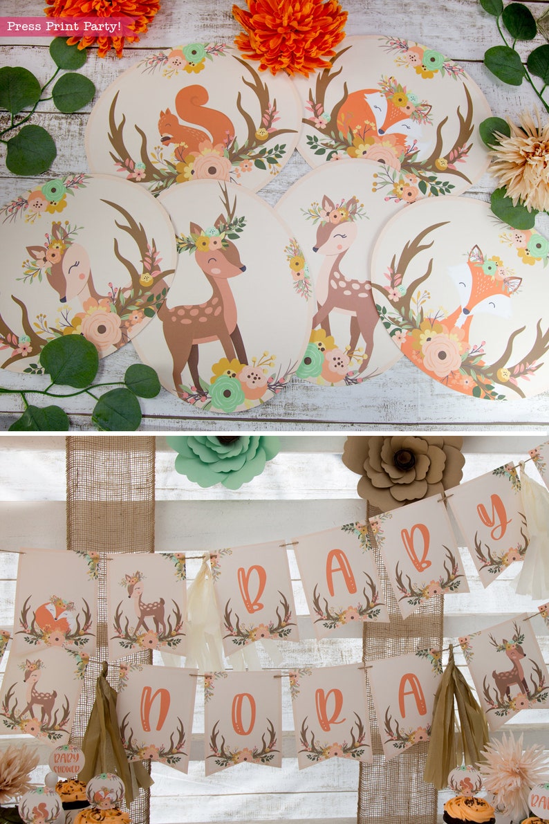 May include: A woodland themed baby shower banner with the word "BABY" in large letters. The banner is decorated with floral patterns, antlers, and deer silhouettes. The banner is strung on a rustic twine.