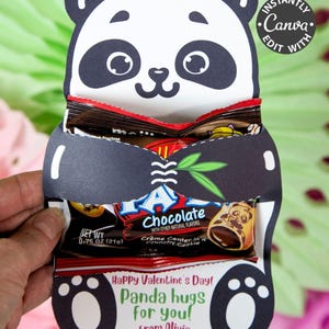 May include: A panda-shaped Valentine's Day card holding chocolate candy bars. The black and white card has the text "Happy Valentine's Day! Panda hugs for you! From Olivia." The card is held by a hand.