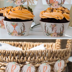 May include: A wicker basket with a banner that reads "BABY" in brown, orange, and green letters. The banner is made of round, floral-patterned paper circles with antlers and a deer or fox design.