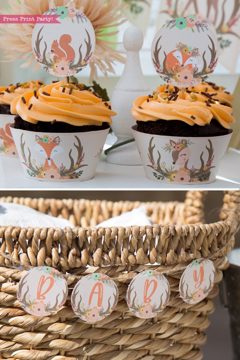 May include: A wicker basket with a banner that reads "BABY" in brown, orange, and green letters. The banner is made of round, floral-patterned paper circles with antlers and a deer or fox design.